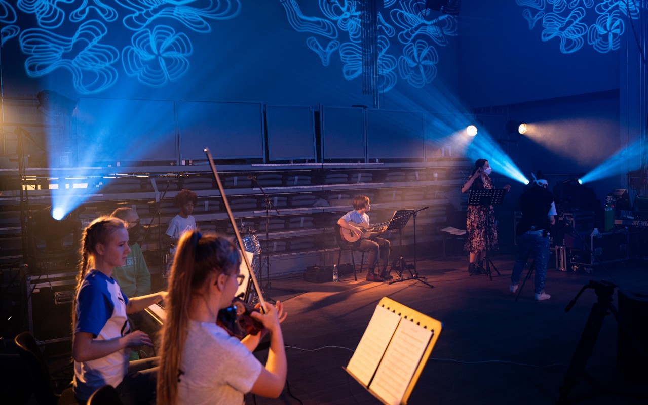 zdjęcie grupy młodzieży grającej na instrumentach w sali oświetlonej zdobnie na niebiesko