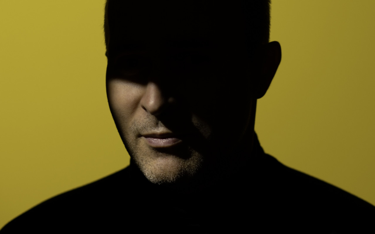 Portret Michała Pepola, twarz ukryta w półcieniu, na jednolitym żółtym tle.